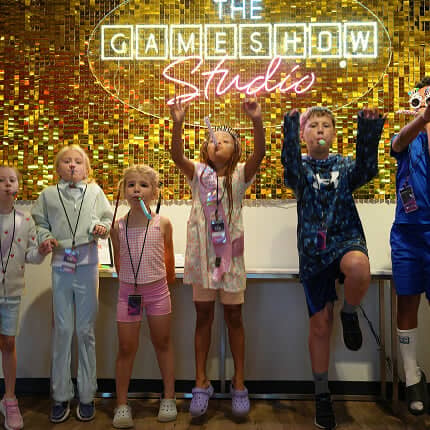 kids in front of neon game show studio sign