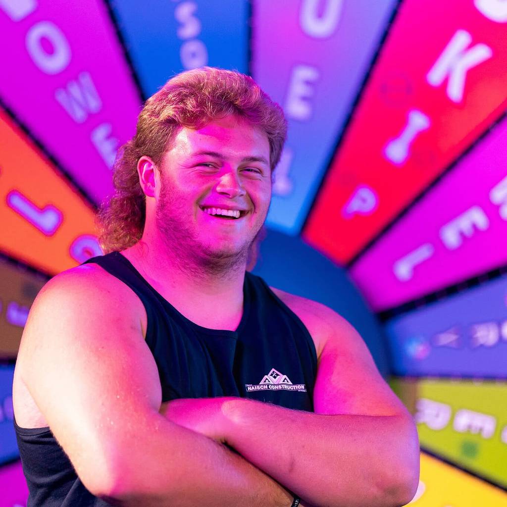 man posing in front of game show wheel